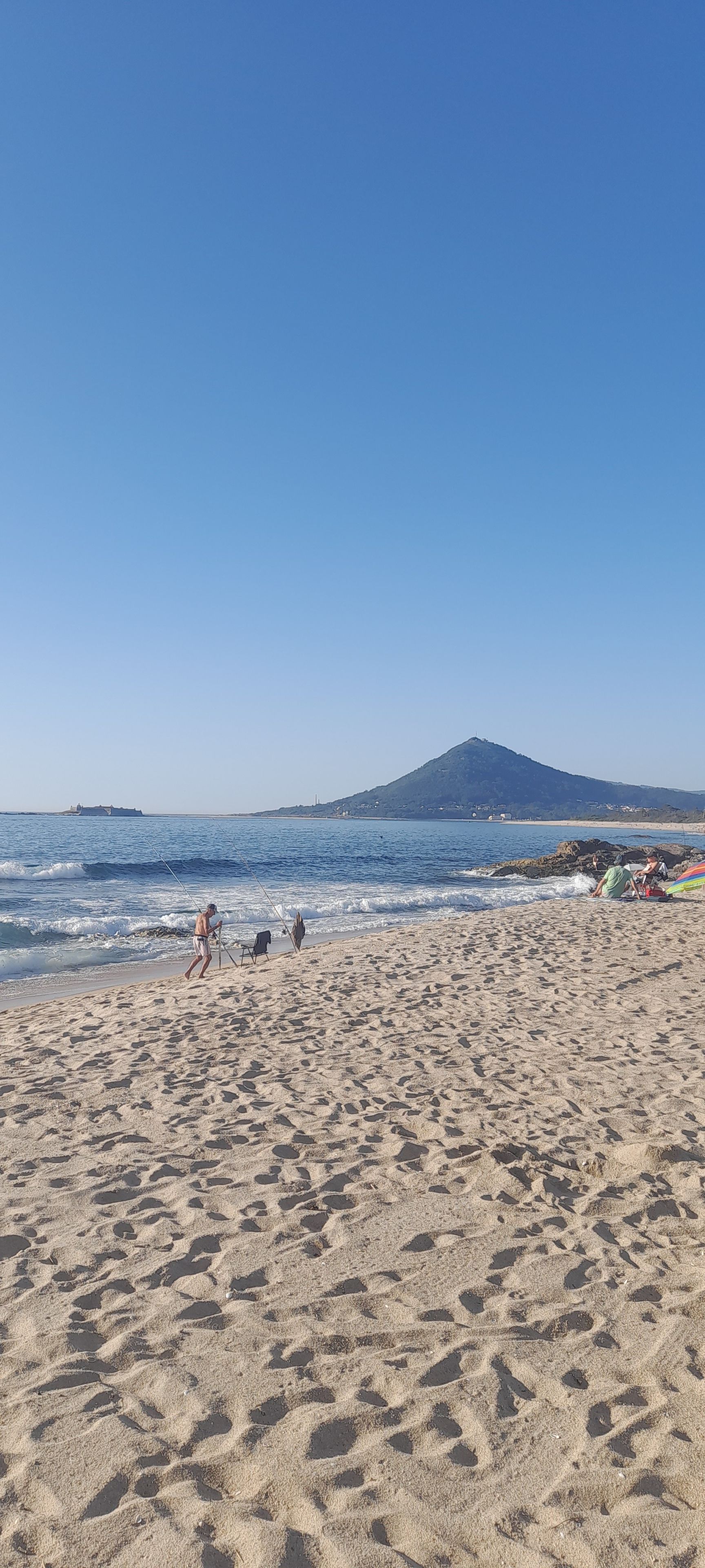 Een zandstrand met een heldere lucht en een berg in de verte.