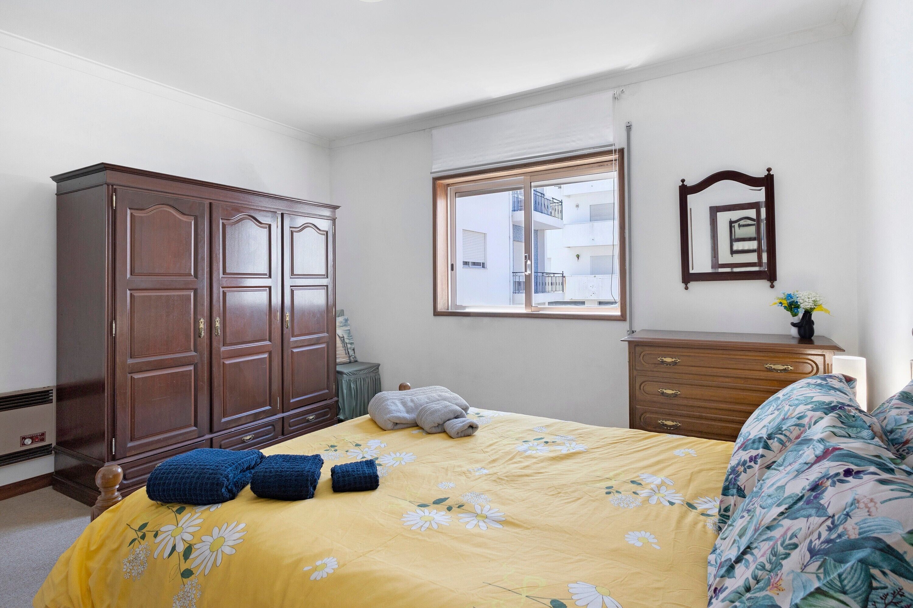 Un dormitorio con cama, armario, cómoda, ventana y espejo.