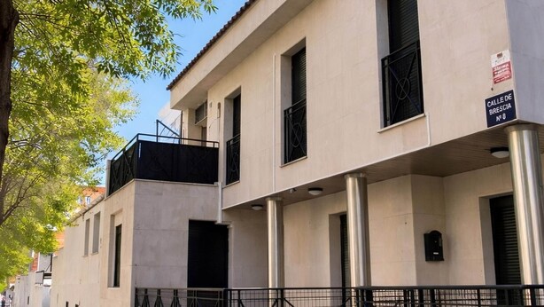 Ein mehrstöckiges Gebäude mit Balkon, Metallzaun und einem Schild mit der Aufschrift 'Calle de Brescia No 6'.