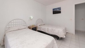 A bedroom with two beds, a ceiling fan, a wall-mounted light, and a painting. - Port Royale 75 - Two Bed (Los Cristianos)