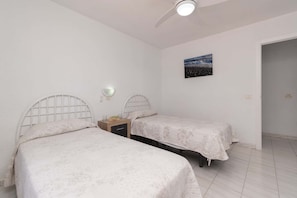 A bedroom with two beds, a ceiling fan, a wall-mounted light, and a painting. - Port Royale 75 - Two Bed (Los Cristianos)