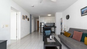 A modern living room with a sofa, coffee table, and a dining area in the background. - Port Royale 75 - Two Bed (Los Cristianos)