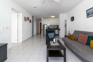 A modern living room with a sofa, coffee table, and a dining area in the background. - Port Royale 75 - Two Bed (Los Cristianos)