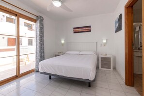 A bedroom with a bed, nightstands, a ceiling fan, and a view through a sliding door. - Port Royale 75 - Two Bed (Los Cristianos)