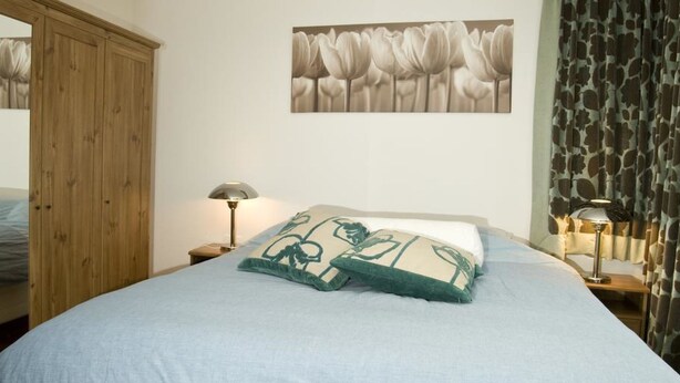 Un dormitorio con cama, mesita de noche, lámpara, armario y un cuadro en la pared.