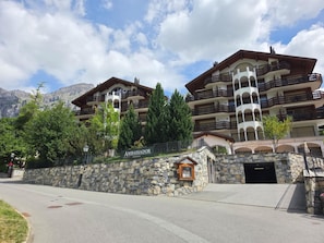 Een hotel met meerdere verdiepingen, balkons, stenen muren en een bergachtig landschap op de achtergrond.