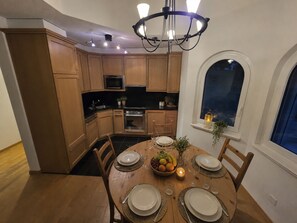 A modern kitchen with wooden cabinets, a central island, and a dining area set for six with a chandelier overhead. - Ambassador B33 # 4-bed apartment, Dusche und Bad, WC by Interhome (Leukerbad)
