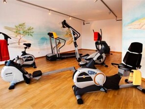 Uma sala de ginástica com bicicletas ergométricas, esteiras e um remo.