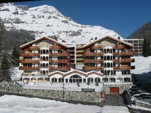 Ein mehrstöckiges Hotel mit Balkonen, einer Stein-Fassade und einem Bergpanorama im Hintergrund.