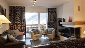 Una sala de estar con sofá, sillón y mesa de centro. Hay chimenea y televisor.