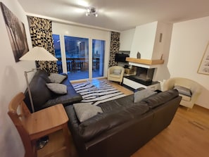 Uma sala de estar moderna com um sofá de couro preto, uma mesa lateral de madeira e uma mesa de centro de vidro.