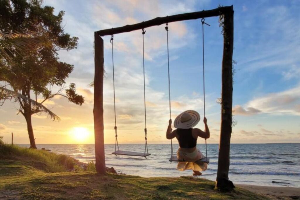 A swing set by the ocean with a sunset in the background.