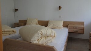 A bedroom with a wooden bed frame, two bedside tables, a wardrobe, and a wall-mounted light fixture. - Fortuna 201 # 4-bed apartment, Dusche, WC 4-Bettwohnung, Dusche, WC by Interhome (Leukerbad)