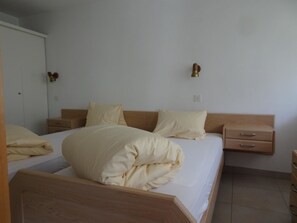 A bedroom with a wooden bed frame, two bedside tables, a wardrobe, and a wall-mounted light fixture. - Fortuna 201 # 4-bed apartment, Dusche, WC 4-Bettwohnung, Dusche, WC by Interhome (Leukerbad)