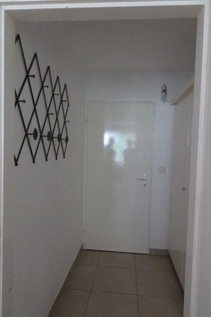 A hallway with a white door, a wall-mounted decorative metal piece, and a light fixture. - Fortuna 201 # 4-bed apartment, Dusche, WC 4-Bettwohnung, Dusche, WC by Interhome (Leukerbad)