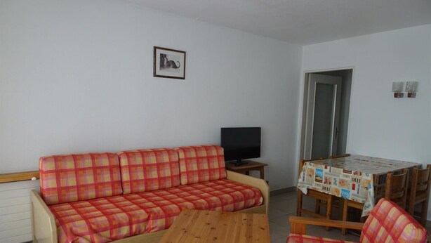 A living room with a sofa, a coffee table, and a television. There is a dining table with chairs and a tablecloth. - Fortuna 201 # 4-bed apartment, Dusche, WC 4-Bettwohnung, Dusche, WC by Interhome (Leukerbad)