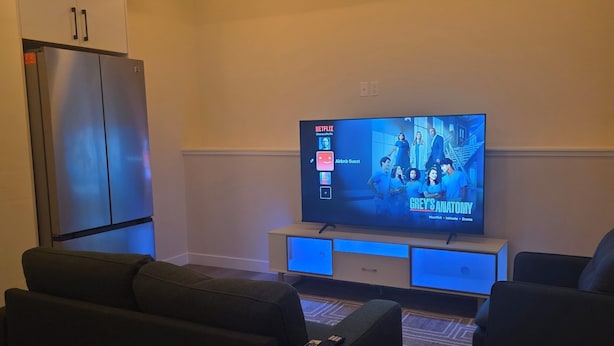 Een woonkamer met een flatscreen-tv, twee banken, een houten vloer en een inbouwkoelkast.