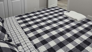 Een slaapkamer met een geruit bedovertrek, een witte handdoek en uitzicht op een keuken met moderne apparaten.