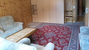 Um quarto com sofá, uma mesinha, tapete vermelho estampado e painéis de madeira nas paredes.