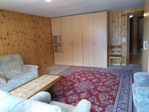 A room with a sofa, a small table, a red patterned rug, and wooden panel walls. - Gassenboden 31 # 4-bed apartment, Bad, WC 4-Bettwohnung, Bad, WC by Interhome (Leukerbad)