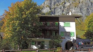 Um edifício de dois andares com uma varanda, um caminhão estacionado na frente e montanhas ao fundo.