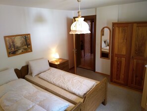 A bedroom with two beds, a bedside lamp, a wooden wardrobe, and a painting on the wall. - Gassenboden 31 # 4-bed apartment, Bad, WC 4-Bettwohnung, Bad, WC by Interhome (Leukerbad)