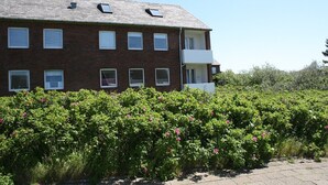 Un edificio in mattoni di più piani con diverse finestre, un balcone e un giardino con fiori rosa.
