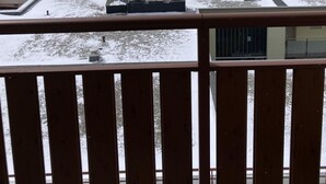 Un patio cubierto de nieve con edificios, vistas a montañas y una barandilla de madera.
