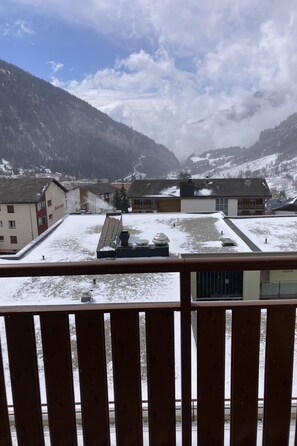 Ein mit Schnee bedeckter Innenhof mit Gebäuden, Blick auf Berge und einem Holzbalkon.