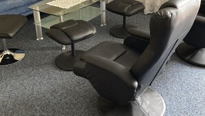 Una habitación con una silla de masaje negra, una mesa de centro de vidrio, un sofá azul con cojines verdes y una lámpara de pie.