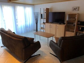 Ein Wohnzimmer mit zwei Sofas, einem Couchtisch, einem Fernseher und einem Bücherregal.