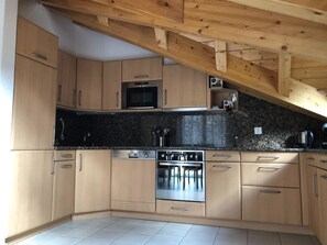 A kitchen with wooden cabinets, a microwave, a stove, and a coffee machine. - Edelweiss B 42 # 6-bed apartment, Dusche und Bad, WC by Interhome (Leukerbad)