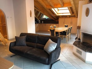Ein modernes Wohnzimmer mit einer schwarzen Ledersofa, einem Essbereich mit rundem Tisch und Stühlen sowie einer Küche mit Holzschränken und einem Oberlicht.