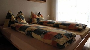 Quarto com duas camas, cada uma com manta acolchoada e almofadas, uma mesa de cabeceira e uma janela com cortinas.