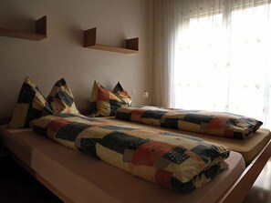 Ein Zimmer mit zwei Betten, jeweils mit gesteppter Decke und Kissen, einem Nachttisch und einem Fenster mit Vorhängen.
