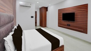 A hotel room with a bed, a TV mounted on the wall, a wardrobe, and an air conditioning unit. - Suite Budha Tower (Noida)
