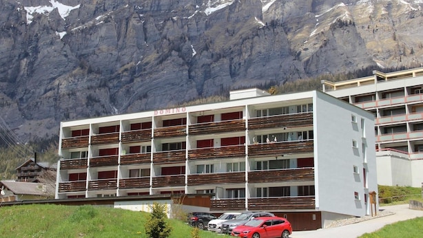 A multi-story building with balconies, a parking area, and a mountainous backdrop. - Domino 15 # 2-bed apartment, Dusche, WC 2-bed apartment, Dusche, WC by Interhome (Leukerbad)