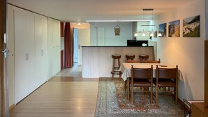 A modern kitchen with a central island, wooden dining table with chairs, and a patterned rug. - Domino 15 # 2-bed apartment, Dusche, WC 2-bed apartment, Dusche, WC by Interhome (Leukerbad)