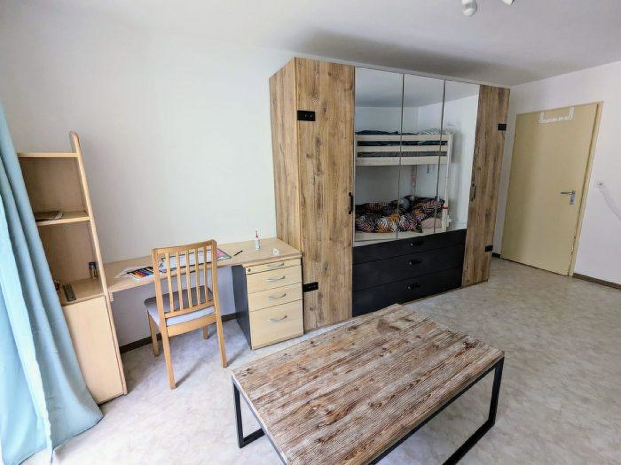 A room with a bed, a desk, a chair, and a wardrobe.