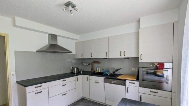 Una cocina moderna con armarios blancos, encimera negra, extractor de acero inoxidable y horno empotrado.