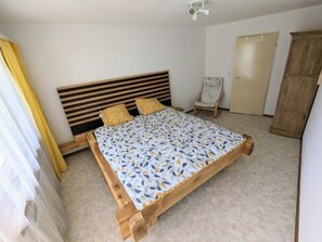 A bedroom with a wooden bed frame, a patterned bedspread, and a chair. - Petit Trianon 103 # 8-bed apartment, Bad, WC 8-bed apartment, Bad, WC by Interhome (Leukerbad)