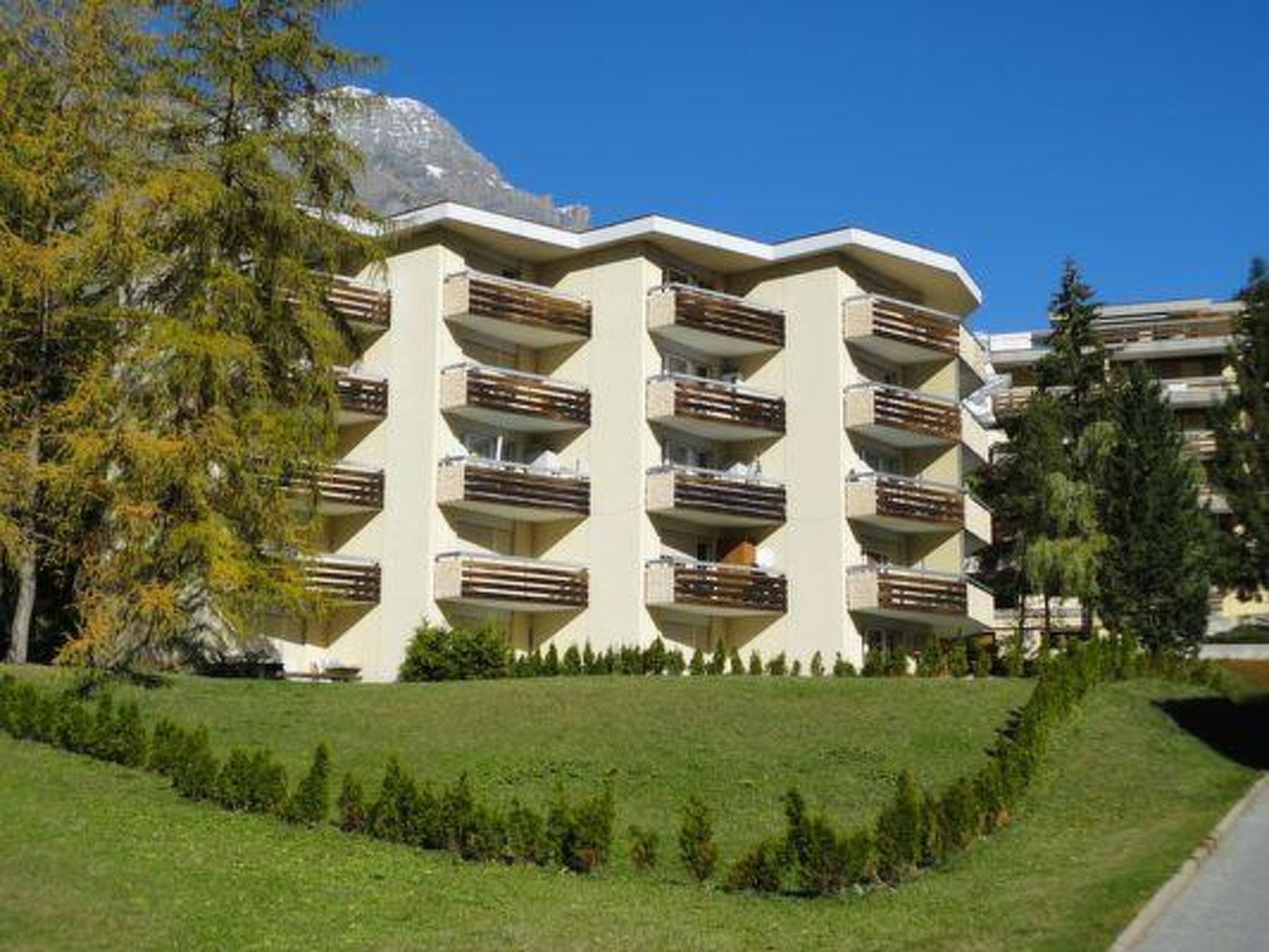 A multi-story hotel with balconies, surrounded by greenery and a mountain backdrop.