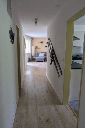 Ein Flur mit Holzboden, der in einen Wohnbereich mit Sofa und Küchenzeile mit Herd führt.