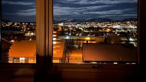 Vista noturna da cidade através de uma janela, com edifícios iluminados e céu limpo.