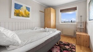 Quarto com cama, guarda-roupa de madeira, janela com vista e um quadro na parede.