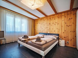 A bedroom with a bed, a bedside table, a lamp, and wooden paneling on the walls. - Brüggli A14 Appartement/Fewo, Bad, WC, 4-Bettwohnung by Interhome (Arosa)