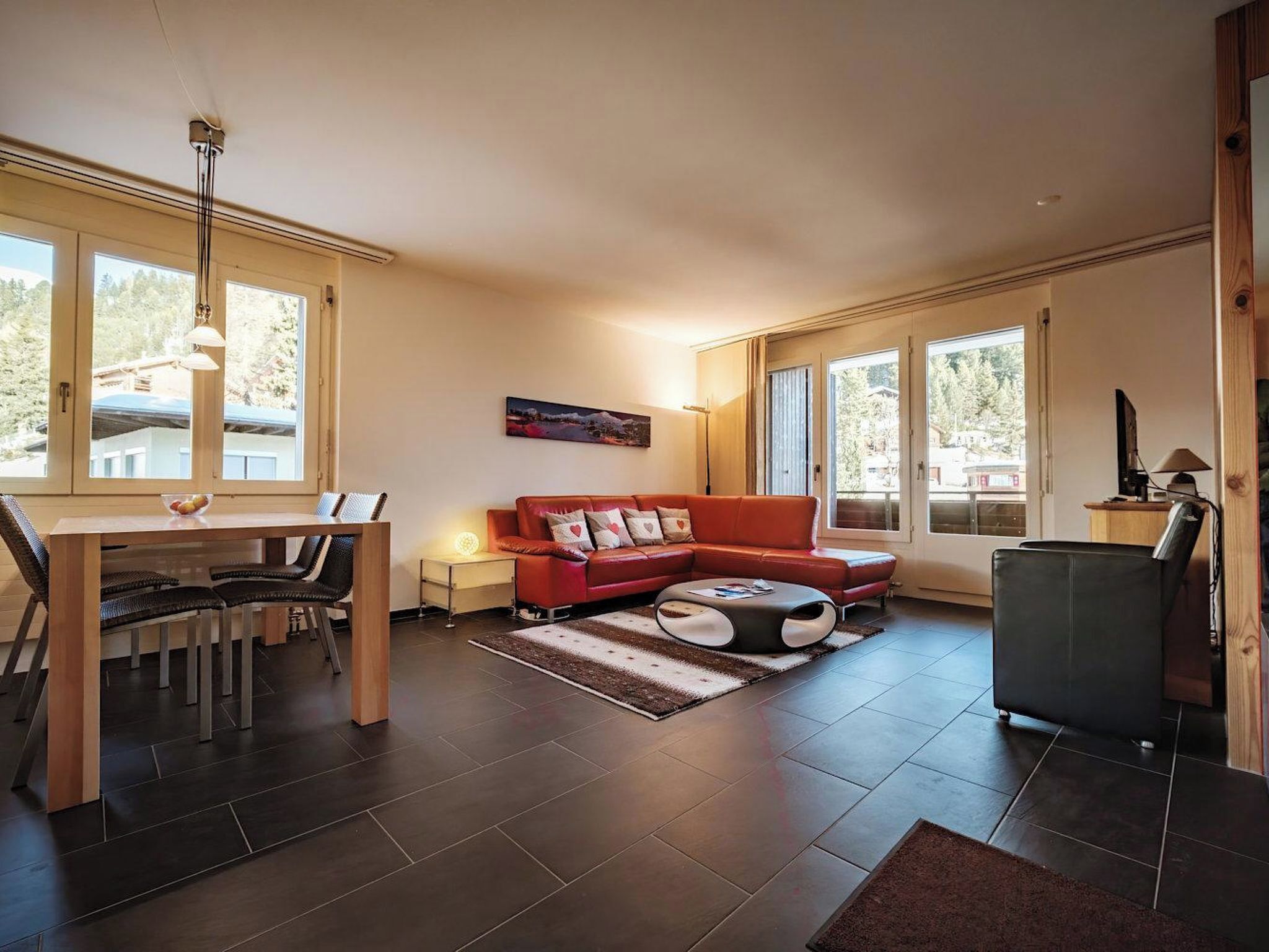 A modern living room with a dining area, large windows, and a view of the outdoors.