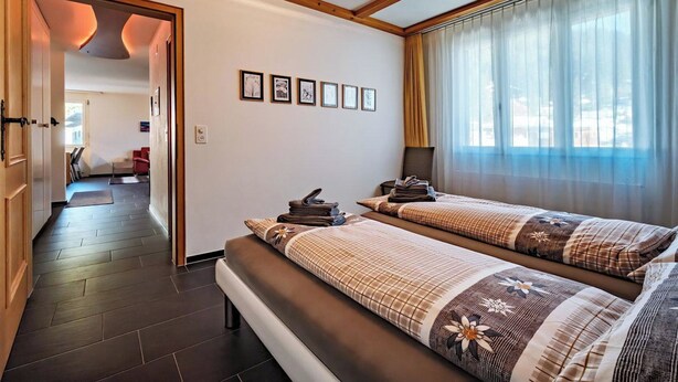 Ein Hotelzimmer mit zwei Betten, einem Flur und Blick ins Freie.