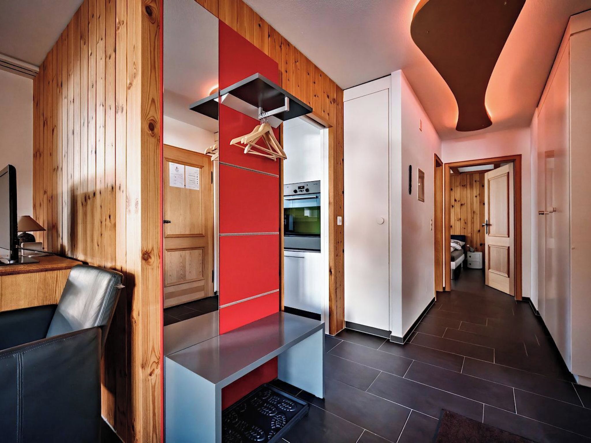 Een moderne keuken met een rode accentmuur, houten lambrisering en een roestvrijstalen afzuigkap.