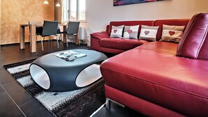 Ein modernes Wohnzimmer mit einem roten Ledersofa, einem runden Couchtisch und einem Essbereich mit Stühlen und einem Tisch.
